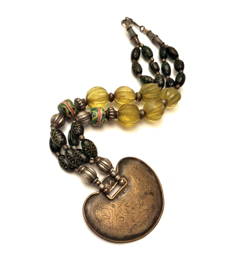 May include: A silver and brass necklace with green and yellow glass beads and a heart-shaped pendant with intricate engravings.