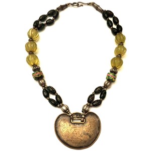 May include: A silver necklace with a heart-shaped pendant. The pendant is decorated with intricate engravings. The necklace is made with green and yellow glass beads.