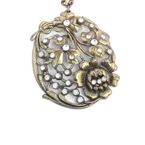 May include: A gold-toned pendant necklace with a floral design featuring a large flower and smaller flowers with rhinestones. The pendant is attached to a chain.