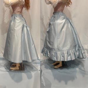 May include: A light blue satin skirt with a ruffled hem, paired with a pink corset. The skirt has a full, flowing shape, and the corset features a lace-up back. The outfit is displayed on a mannequin.