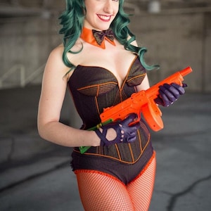 May include: A woman in a black and orange corset with a green wig and orange bunny ears holds an orange toy gun. She is wearing black gloves and fishnet stockings.