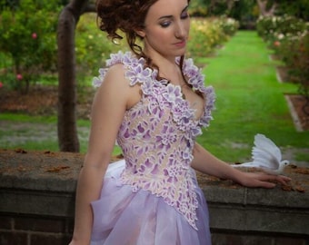 May include: A woman in a purple and white floral corset dress with a white dove perched on a brick wall behind her.