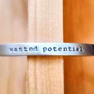 May include: A silver metal bracelet with the words "wasted potential" engraved on it.