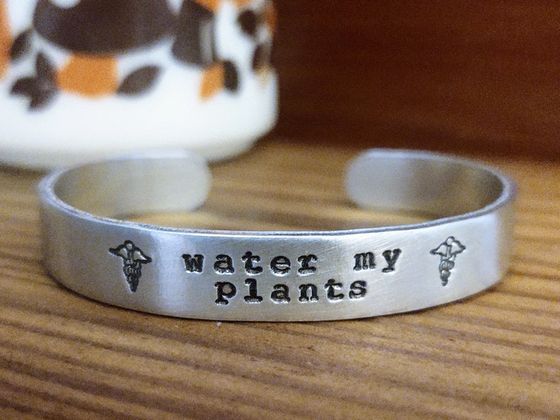 May include: Silver bracelet with the text "water my plants" and a small plant graphic on each side.