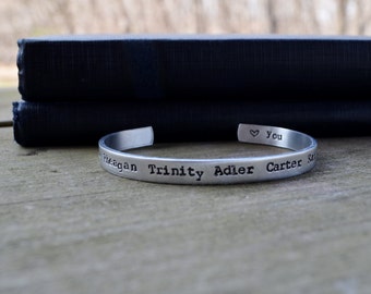 May include: A silver metal bracelet with the names "Reagan", "Trinity", "Adler", "Carter", and "You" engraved on it.