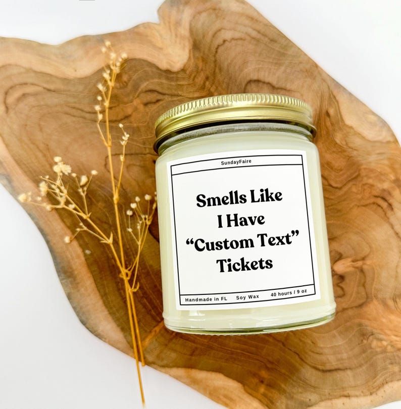 May include: A white candle with a gold lid and a white label that reads "Sunday Faire" and "Smells Like I Have "Custom Text" Tickets". The label also includes "Handmade in FL", "Soy Wax", and "40 hours/9 oz".