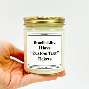 May include: A glass jar candle with a gold lid and a white label. The label reads "Sunday Faire", "Smells Like I Have "Custom Text" Tickets", "Handmade in FL", "Soy Wax", and "40 hours / 9 oz".