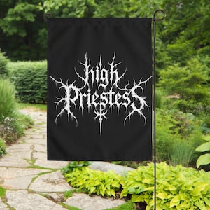 Könnte beinhalten: Eine rechteckige schwarze Gartenflagge mit dem weißen Schriftzug High Priestess in einer stilisierten, dornigen und gezackten Schriftart. Der Schriftzug ist mittig auf dem Stoff platziert, der an einem dünnen schwarzen Metallständer hängt.