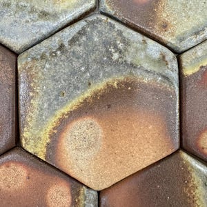 May include: Close-up of a hexagonal tile pattern with a mix of brown, yellow, and gray tones. The tiles have a textured surface and a slightly uneven finish.