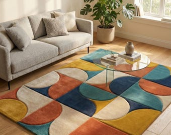 May include: A colorful area rug with a geometric pattern in shades of yellow, orange, teal, and navy blue. The rug is placed on a hardwood floor in a living room setting, with a gray sofa and a glass coffee table.