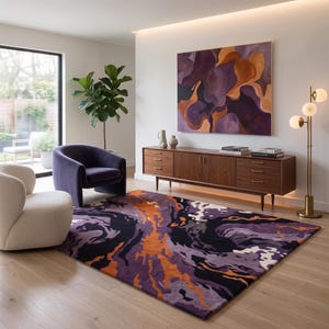 May include: A living room featuring a rectangular area rug with a swirling abstract pattern in shades of purple, orange, black, and white. The room includes a dark purple velvet armchair, a cream-colored chair, and a wooden sideboard with gold hardware.