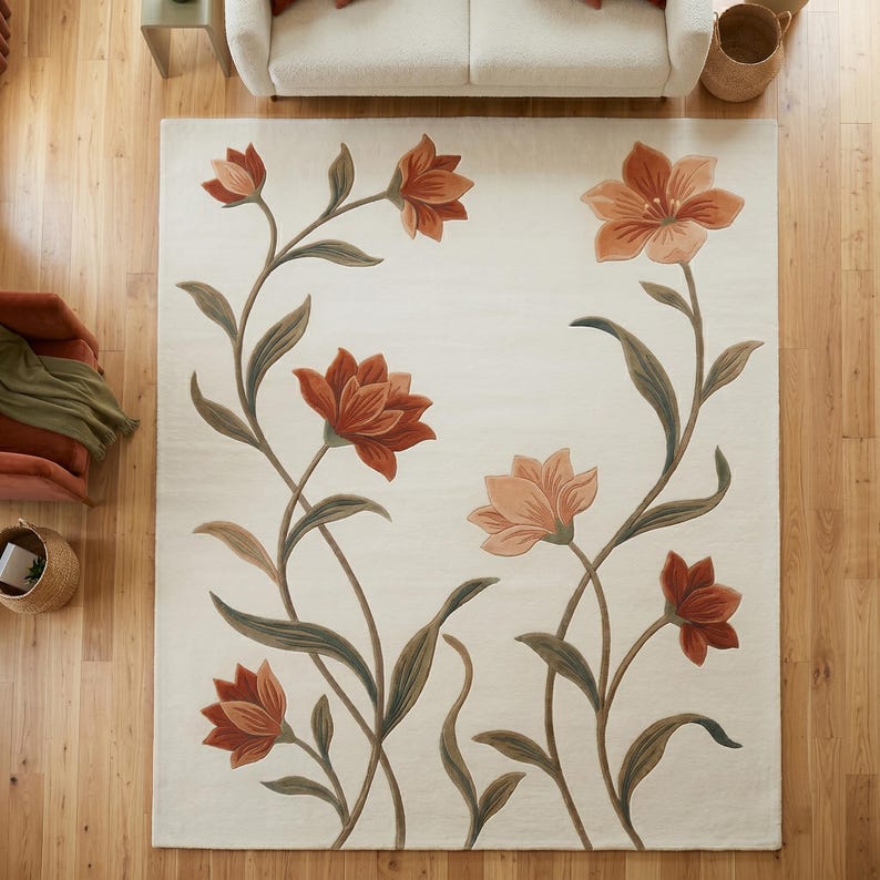 May include: A rectangular area rug with a cream-colored background featuring a large-scale floral pattern. The design includes several blooming flowers in shades of terracotta, rust, and peach, connected by long, curving green stems and leaves.
