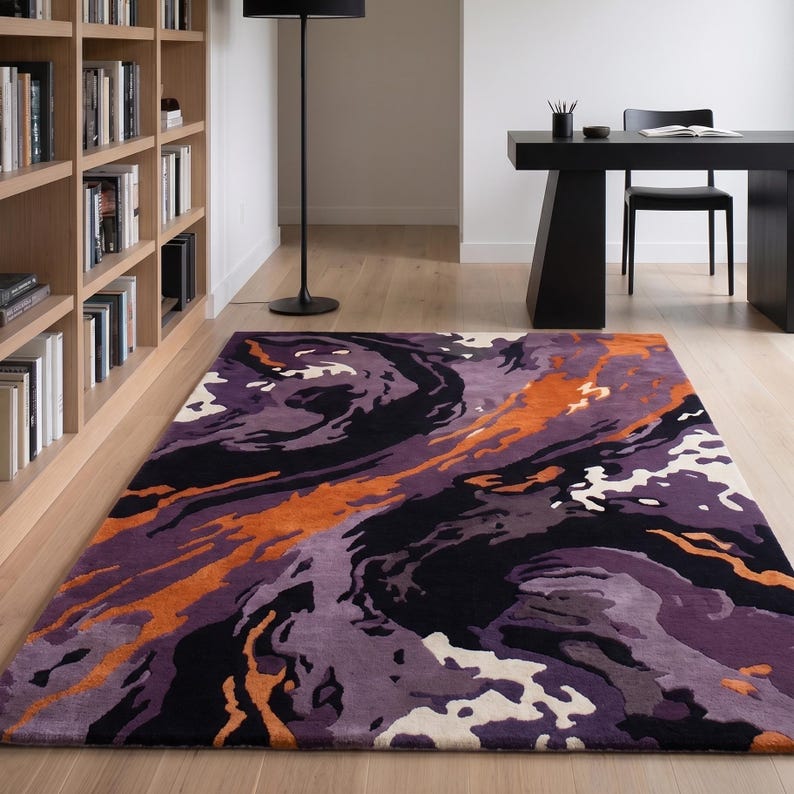 May include: A rectangular area rug featuring an abstract, swirling pattern in shades of deep purple, black, bright orange, and off-white. The design consists of fluid, organic shapes that flow across the surface, creating a bold, high-contrast visual.