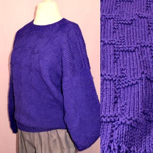 May include: A vibrant purple sweater with a textured, geometric knit pattern. The crew neck sweater features long sleeves and a close-up detail of the knit structure. The sweater is displayed on a mannequin.
