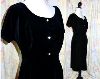 Könnte beinhalten: Ein schwarzes Samtkleid mit kurzen Ärmeln und Knopfleiste. Das Kleid hat ein tailliertes Oberteil und einen leicht ausgestellten Rock.