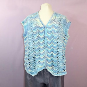 May include: A sleeveless, button-down vest in shades of light blue, white, and pale yellow. The knitted garment features a V-neck and a delicate, openwork pattern. The vest is displayed on a mannequin.