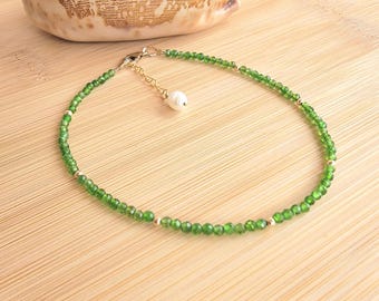May include: A delicate green gemstone anklet with a single pearl charm. The anklet is made of small, faceted green stones and gold beads.