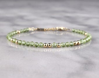 May include: A delicate bracelet featuring small, faceted, light green peridot beads interspersed with gold-colored beads. The bracelet is strung on a thin, gold-colored chain and is designed for a minimalist aesthetic. Jewelry.