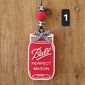 May include: Red and white mason jar ornament with black and white checkered ribbon and red and white checkered beads. The jar has the text "Ball Perfect Mason" on it.