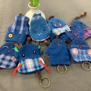 May include: A collection of eight handmade keyrings featuring various animal designs. The keyrings are made from denim and plaid fabric and feature embroidered details. Each keyring has a metal ring for attaching keys.