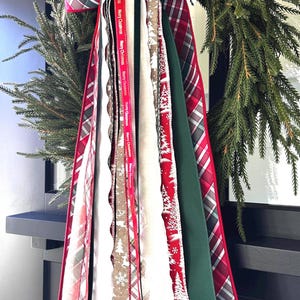 May include: A Christmas wreath with a large plaid bow and cascading ribbons. The ribbons feature various patterns, including Christmas trees, deer, and the text "Merry Christmas". Colors include red, green, white, and brown.