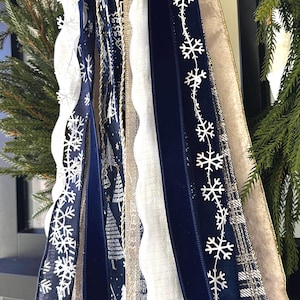 May include: Close-up of decorative ribbons in shades of navy, white, and gold. The ribbons feature snowflake and tree patterns, along with a textured white ribbon and a gold ribbon. The ribbons are part of a holiday decoration.