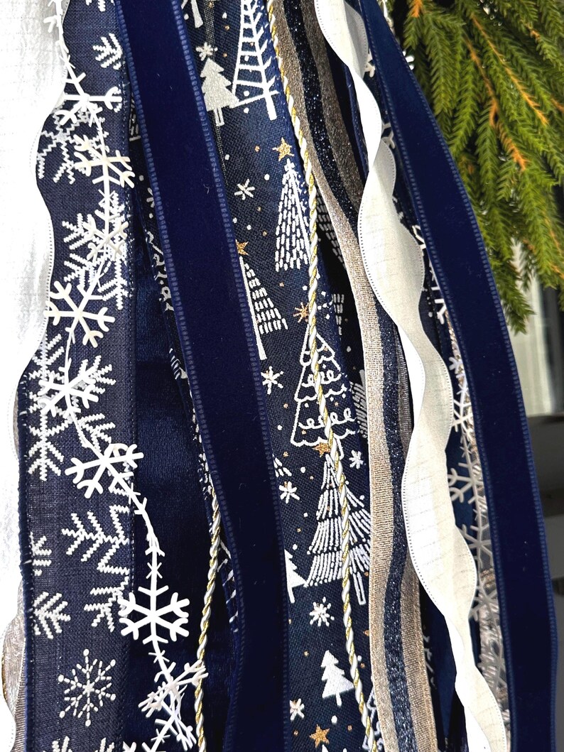 May include: Close-up of decorative ribbons in a winter theme. The ribbons feature snowflake and Christmas tree patterns in white on a navy blue background. Other ribbons include a navy velvet, gold, and white. The ribbons are likely for holiday decor.