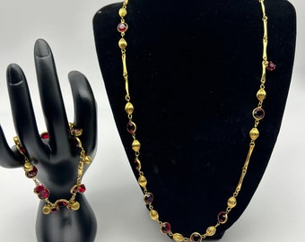 May include: A gold necklace and bracelet set with red glass beads. The necklace is longer than the bracelet and both have a simple chain design.