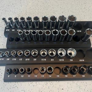 May include: A set of chrome sockets in various sizes, arranged on three black holders. The sockets are labeled with fractional inch measurements, ranging from 5/16 to 15/16 inches. The holders also have numerical markings.