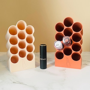 May include: Two lipstick organizers, one beige and one coral, each with multiple circular compartments. A black Revlon lipstick and two lipsticks are placed in the organizers. A lipstick graphic is on the base of each organizer.