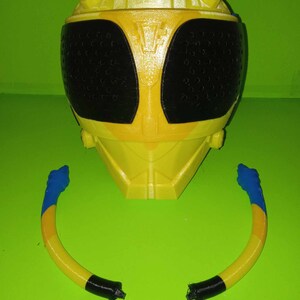 May include: A yellow and black plastic helmet with a black visor and two yellow and blue antennae. The helmet is a toy and is likely part of a costume.