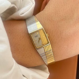 May include: A Pulsar Quartz wristwatch featuring a rectangular gold and silver-tone face with a split design. The dial has a textured silver side and a vertical striped gold side. The matching two-tone metal link bracelet has a repeating pattern.