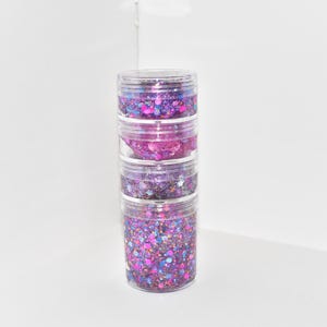 May include: Four clear jars stacked on top of each other, each filled with different colors of glitter. The glitter is a mix of pink, purple, blue, and gold.