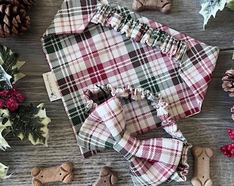 May include: A pet bandana and a matching bow tie, both featuring a red, green, and white plaid pattern. The bandana has a white fabric tag with the text "Chissy's Creations" printed in black. Both items have elasticized bands for attachment.