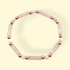 May include: A pink and rose gold bracelet with alternating round and rectangular beads. The bracelet is made of rose gold metal and pink quartz.