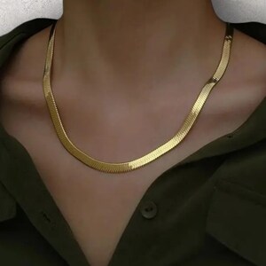 Puede incluir: Un collar de cadena de oro con un diseño de cadena de serpiente.