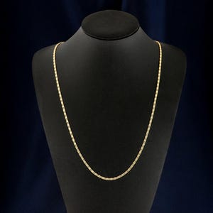 Puede incluir: Un collar de cadena de oro en un expositor negro. La cadena es fina y tiene un diseño delicado de eslabones.