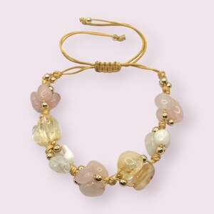 May include: A gold and beige adjustable bracelet with pink, white, and yellow gemstone beads.