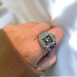 May include: A silver ring with a square watch face. The watch face has black numbers and hands. The ring is set with small clear stones.