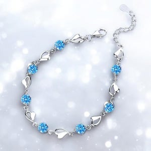 Op de afbeelding: Een zilveren armband met een delicaat hartontwerp en blauwe kristallen accenten.