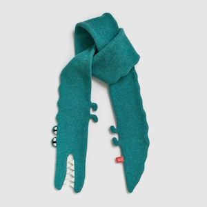 May include: A teal-colored scarf shaped like a crocodile. The scarf features a detailed design with white teeth, black and white eyes, and small, curved appendages. A red tag is attached to the scarf.