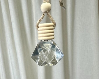 May include: A clear glass diamond-shaped bottle with a wooden cap and a gold and white cord hanging from it.