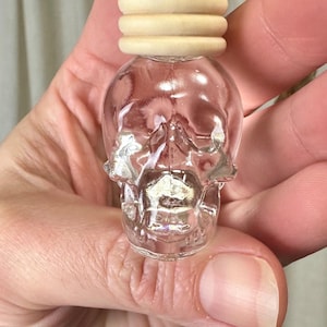May include: A clear glass skull-shaped bottle with a wooden cap and a gold cord. The bottle is hanging from the cord.