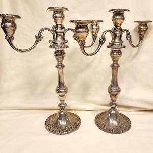 Può includere: Due candelabri argentati con dettagli ornati. Ogni candelabro ha una colonna centrale con una base decorativa e più bracci curvi che sostengono le coppe per candele. La finitura argentata conferisce un aspetto classico ed elegante.