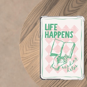 May include: A white tablet case with a green and pink design. The case features the text "LIFE HAPPENS" above an illustration of a hand holding an open book. The words "reading helps" are below the book.