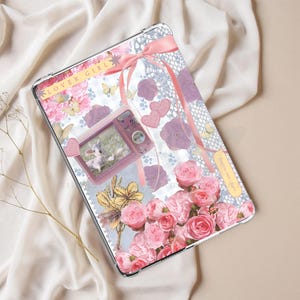 May include: A clear tablet case with a floral design featuring pink roses, butterflies, and a pink ribbon. A small pink camera with a photo is on the case. The text "LOVER GIRL" is visible.