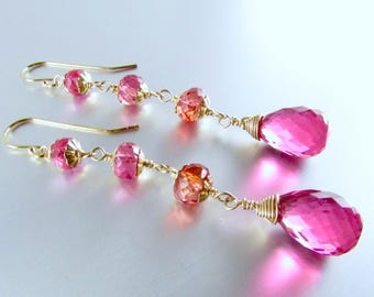 Puede incluir: Un par de pendientes colgantes con piedras preciosas rosas facetadas y cuentas más pequeñas de color naranja-rosa ensartadas en alambre dorado. Los pendientes tienen una piedra preciosa rosa en forma de lágrima en la parte inferior.