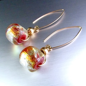Puede incluir: Pendientes de oro con cuentas de vidrio rojo y dorado. Las cuentas tienen un acabado moteado e iridiscente.