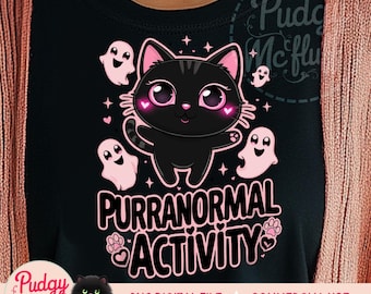 May include: A black t-shirt with a pink graphic of a black cat with big eyes and the text "Purranormal Activity". The graphic also includes pink ghosts and stars.