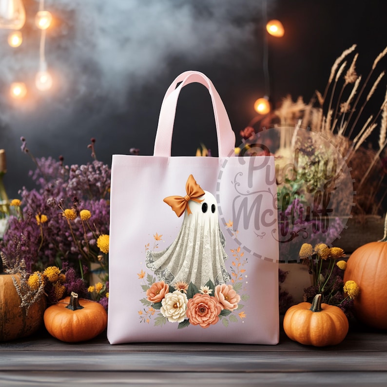May include: A pink tote bag with a ghost wearing a bow and surrounded by flowers. The ghost is white with a lace trim and the flowers are orange and white.